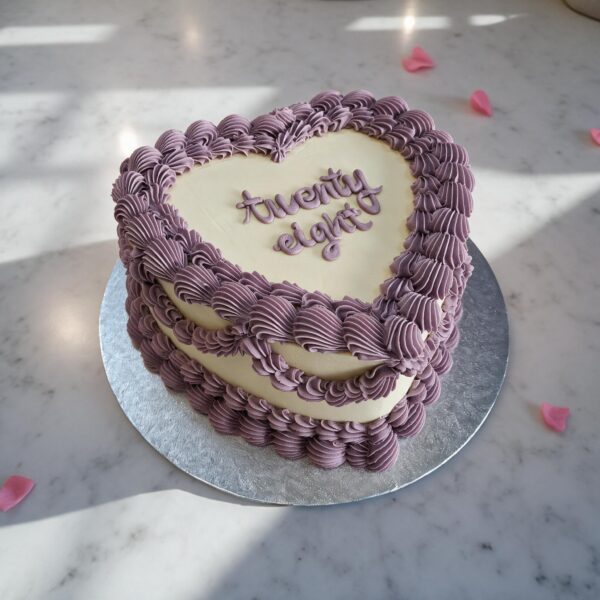 Vintage style heart-shaped cake in ivory with lilac piped borders, "twenty eight" piped in lilac on top